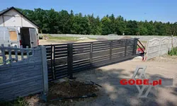 Masywna brama wjazdowa przesuwna między ogrodzeniem betonowym